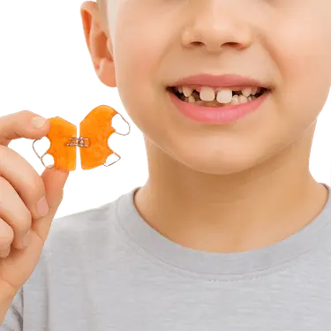 Niño con dentición mixta sosteniendo un aparato de ortodoncia infantil