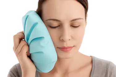 Mujer aplicando frío en la mejilla tras elevación de seno maxilar en recuperación